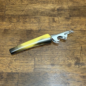 May include: A bottle opener with a yellow and black handle and a silver metal opener. The handle has a gradient effect, transitioning from yellow to black. The opener has a bottle cap remover and a can opener.