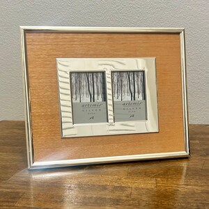 May include: A rectangular double photo frame with a light brown wood-grain border and a polished silver metal frame. The center features two vertical openings with inserts labeled artemis SILVER 2x3 in, displaying a forest photograph.
