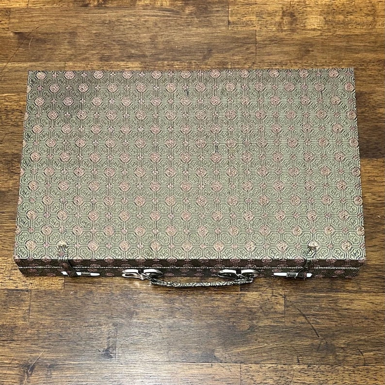 May include: A rectangular, closed case with a patterned fabric exterior. The fabric has a repeating design in shades of green and pink. The case has a silver-colored handle and clasps.