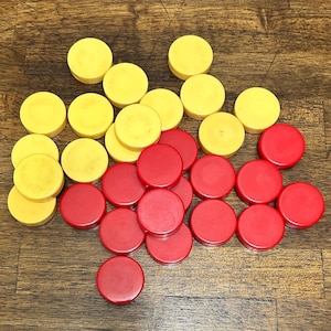 May include: A collection of yellow and red game pieces, likely checkers or similar, scattered on a wooden surface. The pieces are round and flat, with a smooth texture. The yellow pieces are a pale, faded color, while the red pieces are a vibrant, solid color.