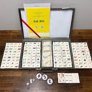 May include: A vintage Mah Jong set with ivory-colored tiles, dice, and counters. The set includes a yellow booklet titled "Standard Rules for the Chinese Domino Game of Mah Jong." The tiles are arranged in a green case.