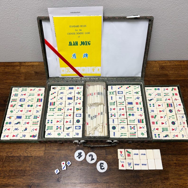 May include: A vintage Mah Jong set with ivory-colored tiles, dice, and counters. The set includes a yellow booklet titled "Standard Rules for the Chinese Domino Game of Mah Jong." The tiles are arranged in a green case.