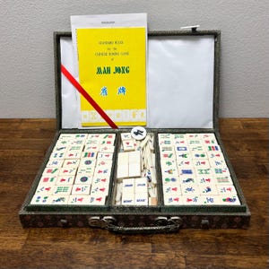 May include: Open Mah Jong set with tiles, dice, and a rule book. The yellow rule book reads "STANDARD RULES for the CHINESE DOMINO GAME of MAH JONG". The set is in a decorative case with a red ribbon.