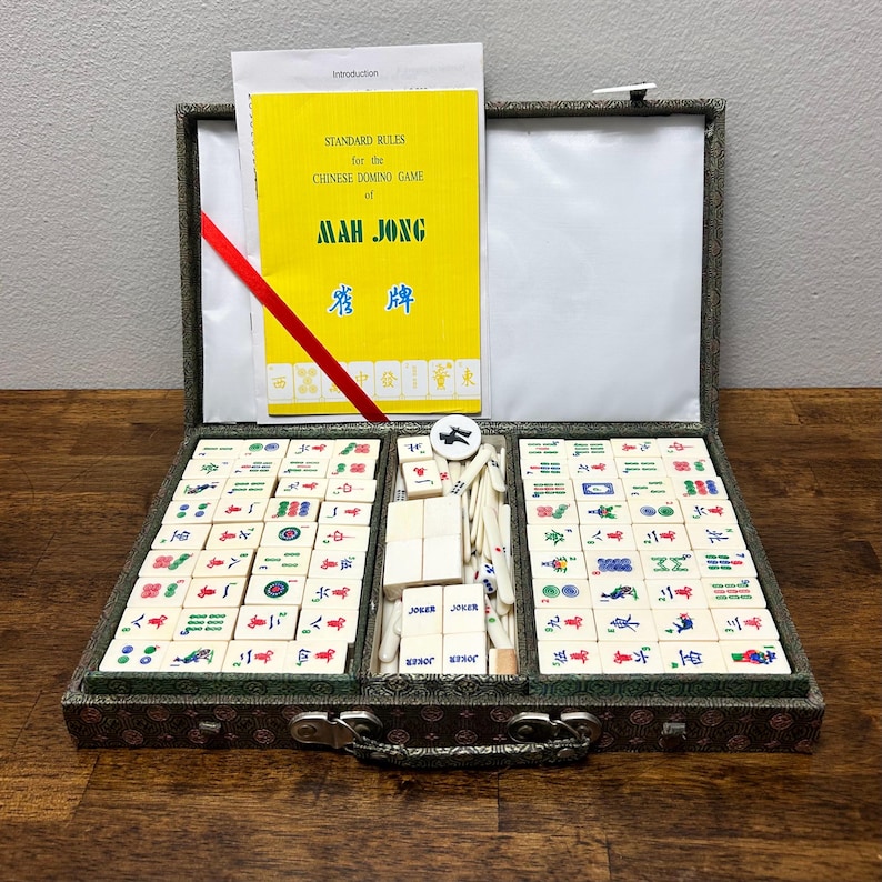 May include: Open Mah Jong set with tiles, dice, and a rule book. The yellow rule book reads "STANDARD RULES for the CHINESE DOMINO GAME of MAH JONG". The set is in a decorative case with a red ribbon.