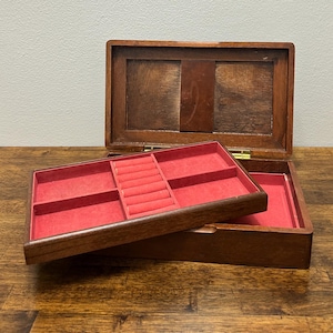 Peut inclure: Une boîte à bijoux en bois avec un couvercle à charnière et un intérieur doublé de velours rouge. La boîte comporte plusieurs compartiments et des fentes pour bagues. La boîte ouverte révèle un plateau avec des fentes et des compartiments pour bagues.