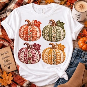 Op de afbeelding: Een wit T-shirt met korte mouwen en een grafische print van vier pompoenen in oranje, groen, bordeauxrood en geel. Elke pompoen heeft een patroon van bloemmotieven, vichy-ruitjes en strepen, vergezeld door gedetailleerde herfstbladeren.