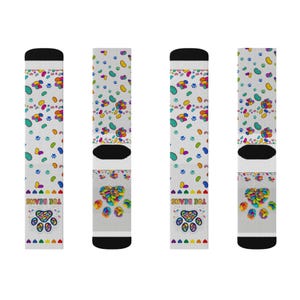 May include: A pair of white crew socks featuring a repeating pattern of colorful jelly bean-shaped paw prints and small paw outlines. The lower section displays a large paw print graphic filled with jelly beans and the text TOE BEANS.