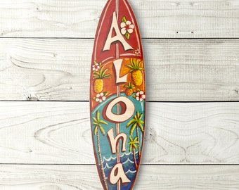 May include: A red, orange, and blue surfboard with the word "ALOHA" painted on it. The surfboard is decorated with pineapples, palm trees, and flowers.