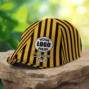 Peut inclure: Une casquette plate ornée d'un motif de rayures verticales noires et jaunes. Le panneau avant présente un écusson blanc circulaire avec le texte noir YOUR LOGO HERE et le texte cursif noir Custom Text situé juste sous l'écusson.
