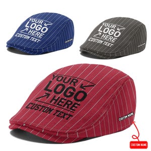 Puede incluir: Tres gorras planas a rayas en azul, gris y rojo. Cada gorra presenta el texto impreso YOUR LOGO HERE CUSTOM TEXT y una pequeña etiqueta lateral que dice CUSTOM NAME. La gorra roja incluye una flecha roja señalando la etiqueta con una marca.