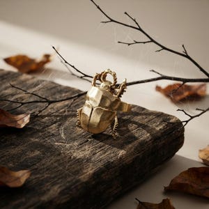 Peut inclure: Une bague dorée représentant un scarabée détaillé. L'insecte possède une carapace lisse et arrondie ainsi que des pattes articulées, avec un anneau simple fixé sous le corps de l'insecte, présentant une finition métallique.
