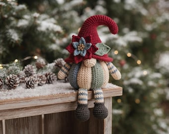 Può includere: Una statuetta di gnomo all'uncinetto con un alto cappello a punta rosso scuro decorato con un fiore blu e rosso. Lo gnomo ha un corpo rotondo beige con strisce verticali in blu, verde e crema, e gambe a righe penzolanti con piedi di colore scuro.