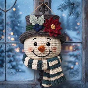 Pu&ograve; includere: Una decorazione da parete all'uncinetto a forma di pupazzo di neve con testa color crema, cilindro grigio scuro decorato con una stella di Natale rossa, foglie verdi e bacche blu, e una sciarpa a righe verde scuro e crema con occhi neri.