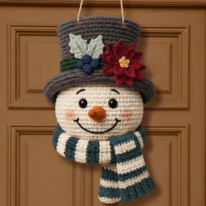Può includere: Una decorazione da parete all'uncinetto a forma di pupazzo di neve con testa color crema, sorriso nero ricamato, occhi neri e naso arancione. Indossa un cilindro grigio scuro decorato con una stella di Natale rossa, foglie verdi e bacche blu.