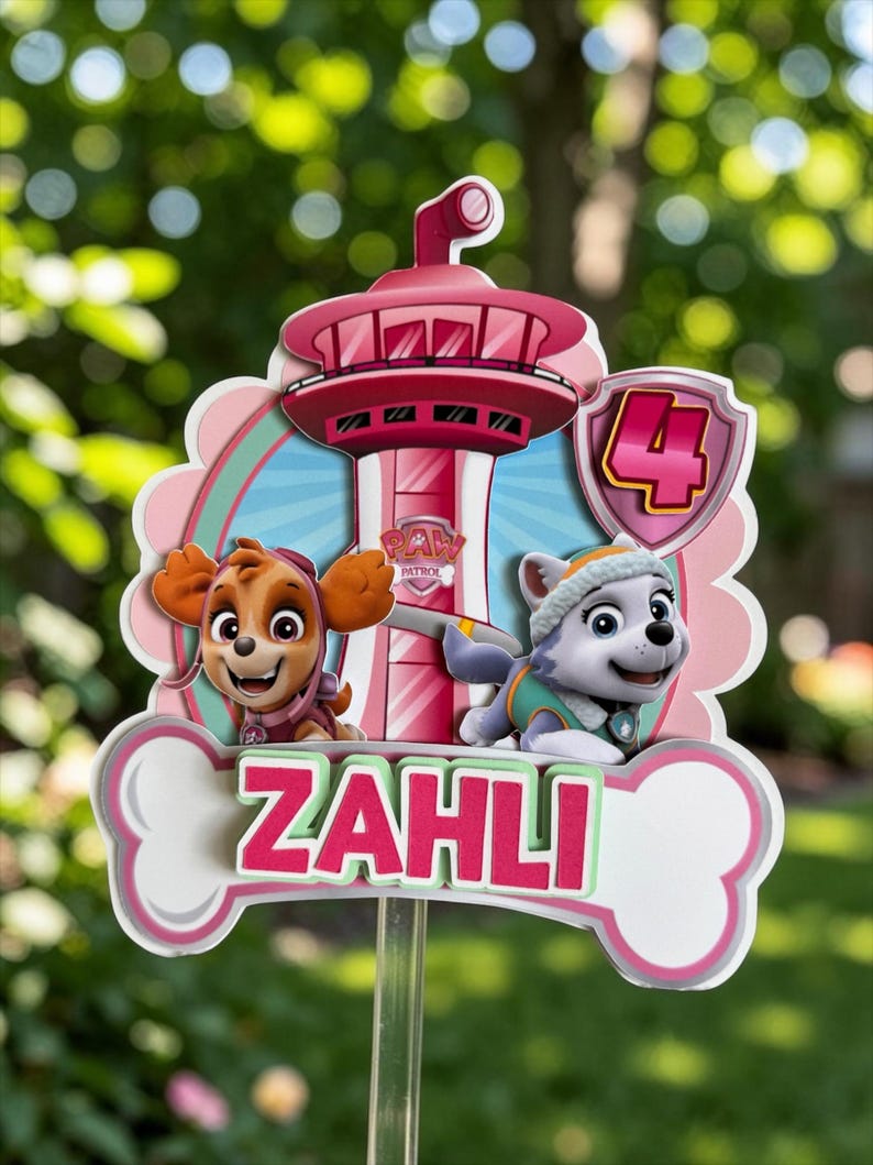 May include: A Paw Patrol themed cake topper featuring a pink lookout tower, the characters Skye and Everest, and a shield with the number 4. A white bone-shaped cutout at the bottom displays the name ZAHLI in bold pink letters.