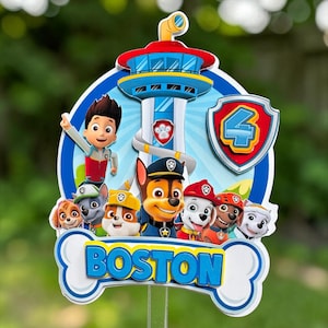 May include: A Paw Patrol themed cake topper featuring a central lookout tower, the character Ryder, and a group of puppies. The design includes a shield with the number 4 and a white bone-shaped base with the name BOSTON printed in blue letters.