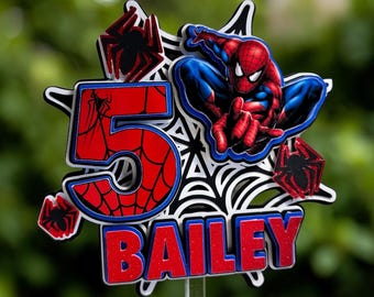 May include: A layered cake topper featuring a red and blue number 5 with a spiderweb pattern, a red and blue Spider-Man figure, three small red glittery spiders, and the name BAILEY in red glittery letters, all mounted on a clear plastic stick.