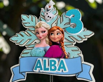 May include: A cake topper featuring a large glittery light blue snowflake, the characters Elsa, Anna, and Olaf, a glittery blue number 3, and a light blue banner with the name ALBA in glittery blue letters, all mounted on a thin stick.