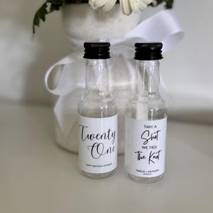 May include: Two clear glass miniature bottles with black screw caps, each featuring a white label. One label reads Twenty One Happy Birthday Monique, and the other reads Take A Shot We Tied The Knot Tahlia + Anthony 24.05.26, both in black script.