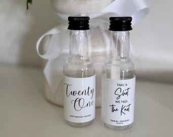 May include: Two clear glass miniature bottles with black screw caps, each featuring a white label. One label reads Twenty One Happy Birthday Monique, and the other reads Take A Shot We Tied The Knot Tahlia + Anthony 24.05.26, both in black script.