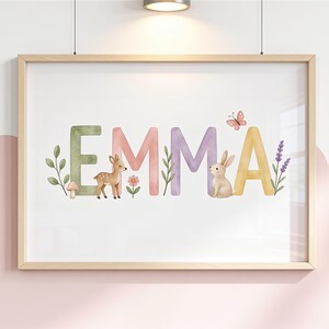 Könnte beinhalten: Ein gerahmter Wanddruck mit dem Namen EMMA in großen, farbenfrohen Buchstaben im Aquarellstil. Das Design zeigt ein kleines braunes Rehkitz, einen hellbraunen Hasen, eine rosa Blume, einen Schmetterling und grüne Pflanzenzweige.