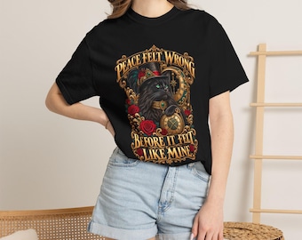 May include: A black short-sleeve t-shirt featuring a graphic of a black cat wearing a top hat and holding a pocket watch, surrounded by red roses and gold filigree. The text reads, PEACE FELT WRONG BEFORE IT FELT LIKE MINE.
