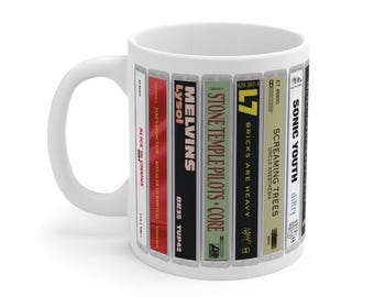 Puede incluir: Una taza de cerámica blanca con un estampado gráfico envolvente de varios lomos de casetes de música. El diseño incluye títulos como Alice in Chains Dirt, Jane's Addiction Ritual de lo Habitual, Melvins Lysol, Stone Temple Pilots Core, L7 Bricks Are Heavy, Screaming Trees Uncle Anesthesia y Sonic Youth Dirty.