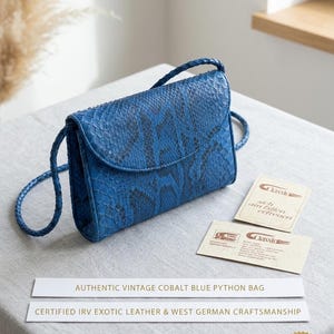 May include: A cobalt blue python skin handbag with a braided shoulder strap and a flap closure. Included are two informational cards with the text Classic, sich am Edlen erfreuen, and Certified IRV Exotic Leather & West German Craftsmanship.