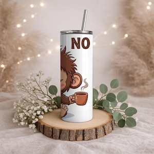 Op de afbeelding: Een witte cilindrische beker met een metalen rietje met een cartoonillustratie van een bruine aap die een dampende bruine koffiemok vasthoudt. Het woord NO is in grote bruine hoofdletters boven de aap gedrukt. De beker heeft een deksel.