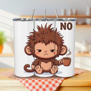 Può includere: Un bicchiere cilindrico bianco con cannuccia in metallo, caratterizzato da un'illustrazione a cartone animato di una scimmia bruna imbronciata con pelo spettinato che tiene una tazza di caffè fumante. La parola NO è stampata in marrone.