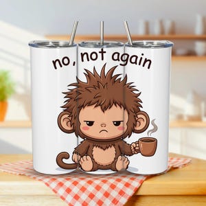 Può includere: Un bicchiere cilindrico bianco con cannuccia e coperchio in metallo, raffigurante un'illustrazione a cartone animato di una scimmia bruna imbronciata con i capelli spettinati che tiene una tazza di caffè. Il testo "no, not again" è in nero.