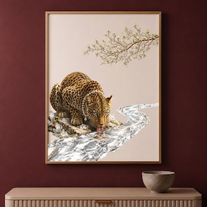 May include: A framed wall art print featuring a leopard with bright blue eyes and a pearl necklace, crouching on a rock formation. The leopard is drinking from a winding, crystalline stream, with a delicate flowering branch above the animal.