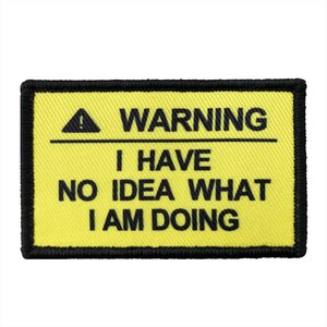 May include: A rectangular embroidered patch with a bright yellow background and a thick black border. The text WARNING appears at the top with an exclamation mark icon, followed by the text I HAVE NO IDEA WHAT I AM DOING in black.