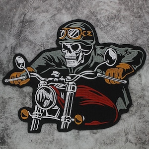 May include: An embroidered patch featuring a skull wearing a helmet with goggles, riding a motorcycle. The skull is gray and white, the helmet is dark gray, the goggles are orange, and the motorcycle has a red fuel tank and orange turn signals.
