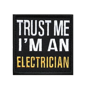 May include: A square black embroidered patch with a stitched border. The text reads TRUST ME I'M AN in white capital letters on the top two lines, and the word ELECTRICIAN in yellow capital letters on the bottom line, all in a sans-serif font.