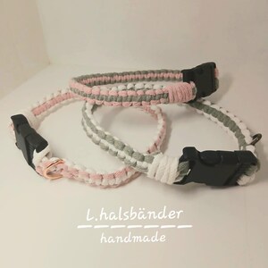 Puede incluir: Dos collares para mascotas hechos a mano con cordón trenzado en tonos rosa, verde salvia y blanco. Cada collar cuenta con una hebilla de plástico negra de liberación lateral y una anilla en D metálica. El texto L.halsbänder handmade aparece debajo.