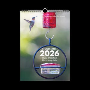 May include: A 2026 calendar featuring a ruby-throated hummingbird. The calendar has a metal hanger and a blue and red hummingbird feeder. The text "Photography by Jim Wright" is visible.