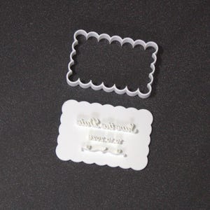 May include: A white rectangular cookie cutter with a scalloped edge and a matching white stamp featuring the embossed text "Save the Date", the date "10.10.2026", and a small decorative line with two hearts centred below the date.
