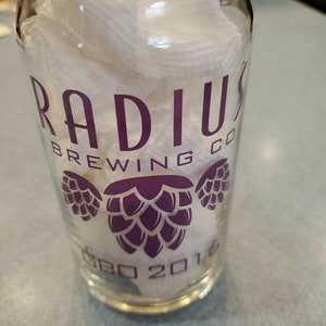 May include: A clear glass with a purple logo that says "Radius Brewing Co. Est. 2016" with three purple hop cones on the front.