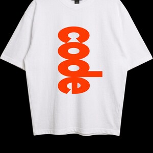Puede incluir: Una camiseta blanca de manga corta con la palabra code impresa verticalmente en letras de color naranja brillante en el centro. La prenda tiene un cuello redondo y una etiqueta de la marca Gildan visible en el interior del cuello.