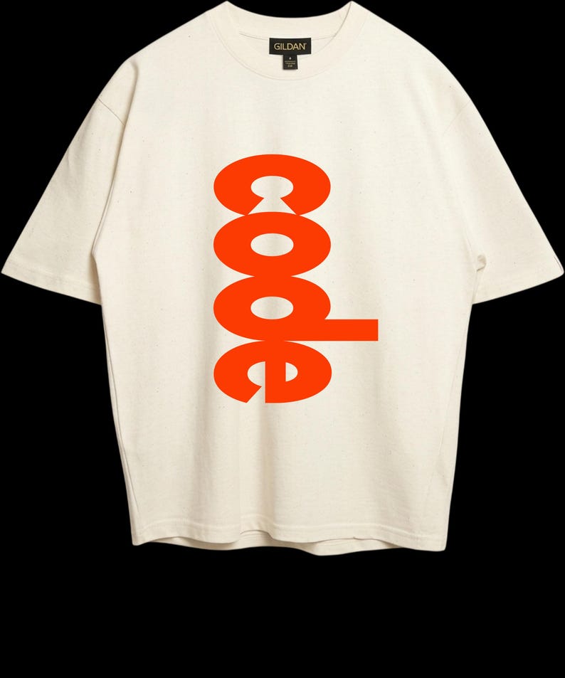 Puede incluir: Una camiseta de manga corta de color crema con la palabra code impresa en una fuente naranja brillante y negrita verticalmente en el centro del pecho. La prenda tiene un cuello redondo y una etiqueta de la marca Gildan visible en el interior.