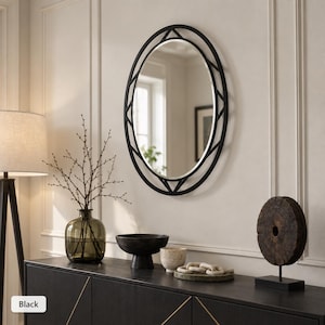 May include: An oval wall mirror featuring a black frame with a geometric, open-work design. The mirror has a smooth, reflective surface and is mounted on a wall. The frame consists of a thin outer oval and an inner oval connected by triangular metal accents.