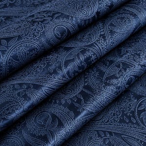 Puede incluir: Una tela azul marino oscuro con un patrón de cachemira en relieve tono sobre tono. El material está doblado en capas diagonales, resaltando los intrincados motivos repetitivos en forma de lágrima y detalles florales que crean una superficie texturizada.