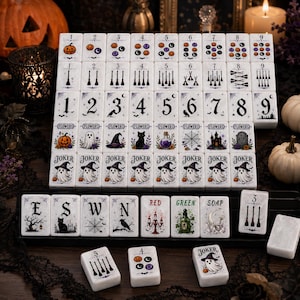 Może przedstawiać: Zestaw białych prostokątnych płytek do mahjonga z ilustracjami o tematyce Halloween, takimi jak dynie, duchy, czarne koty, kapelusze czarownic, miotły i pająki. Płytki zawierają cyfry od jednego do dziewięciu, słowo Joker oraz litery E, S, W, N.