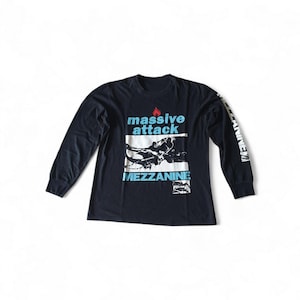 May include: A black long-sleeve shirt featuring a graphic print on the chest with the text "massive attack" in light blue, a small red flame icon, and the word "MEZZANINE" in light blue. The sleeve features the text "MEZZANINE" in white.