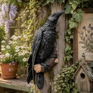 以下が含まれることがあります： 質感のある茶色の枝にとまった黒いカラスの彫刻。鳥は詳細な羽の模様と鋭い嘴を特徴とし、垂直の木の柱に取り付けられています。彫刻はマット仕上げの暗い色で、リアルな鳥の解剖学的構造と集中した姿勢を示しています。
