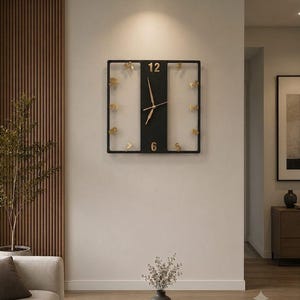 Puede incluir: Un reloj de pared cuadrado con marco negro y un panel central vertical negro. La esfera tiene manecillas doradas y números dorados en las posiciones 12, 6 y 5, con detalles dorados adicionales colocados alrededor del perímetro.