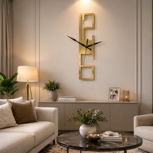 May include: A vertical wall clock featuring a gold-coloured metal frame with an open, geometric rectangular design. The clock has thin black hands positioned at the centre of the frame, contrasting against the metallic gold finish of the structure.
