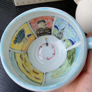 Pode incluir: Uma chávena de cerâmica branca com ilustrações pintadas à mão no interior, inspiradas nas obras de Vincent van Gogh. A taça apresenta painéis segmentados com cenas coloridas, incluindo um retrato, uma paisagem e uma figura.