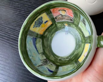 Può includere: Una tazza in ceramica con esterno bianco e interno verde, caratterizzata da riproduzioni in miniatura dipinte a mano di famose opere d'arte, tra cui un ritratto, un vaso di fiori e un paesaggio, disposte lungo le pareti interne.